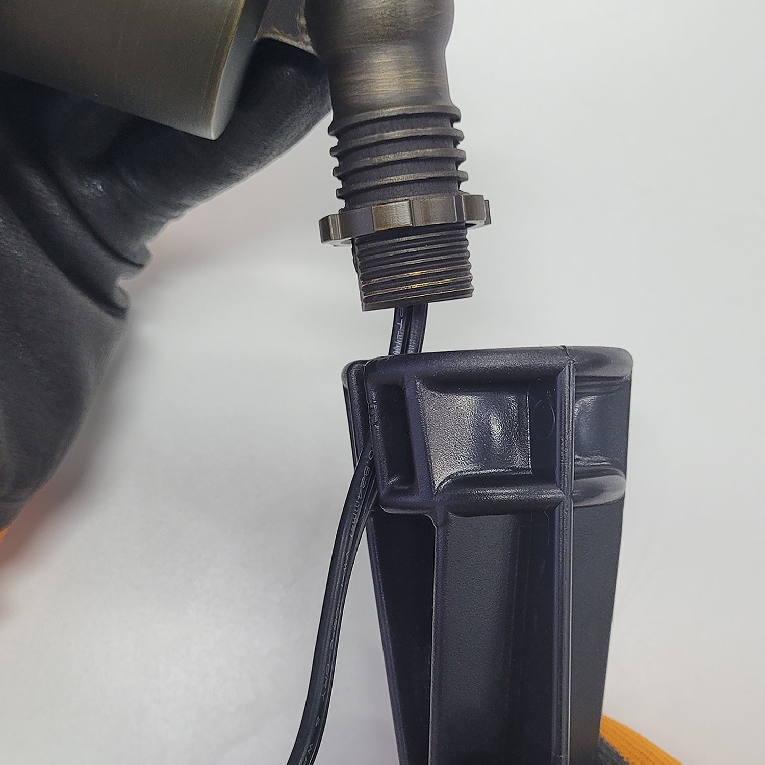 Close-up of PVC landscape light ground stake with cable and threaded connector held by gloved hand for outdoor lighting installation