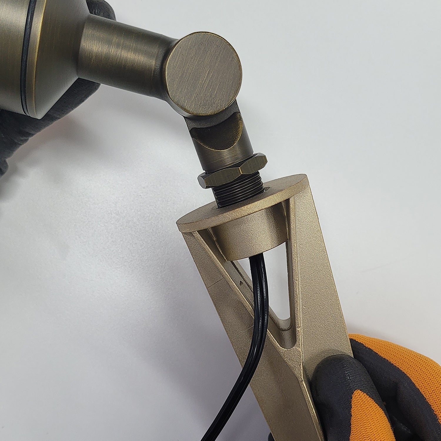 Detail of brass landscape light fixture with ground stake and wiring, held by gloved hand