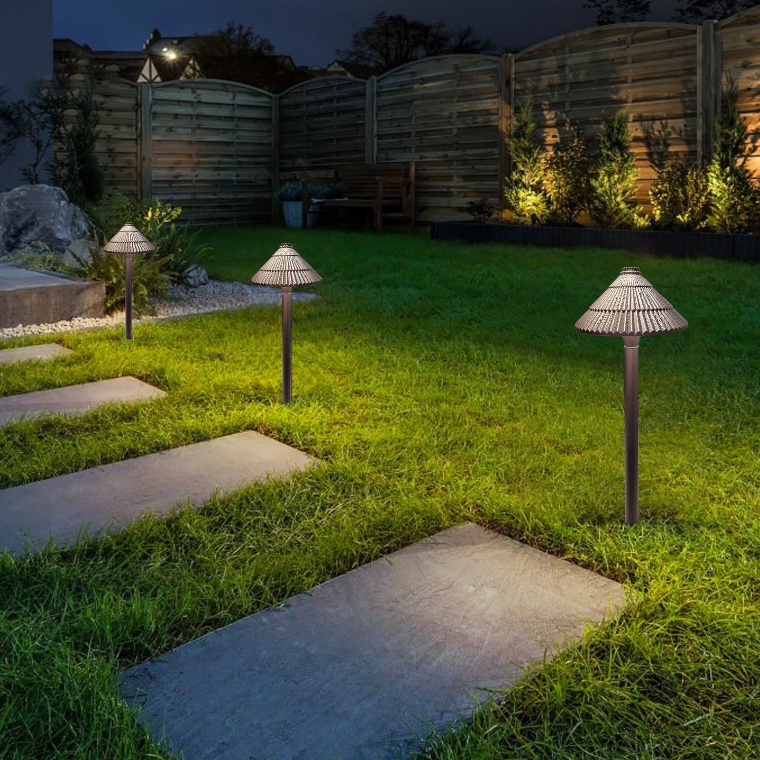 Nighttime garden scene with solid brass low voltage path lights illuminating a stone slab walkway, surrounded by grass and plants