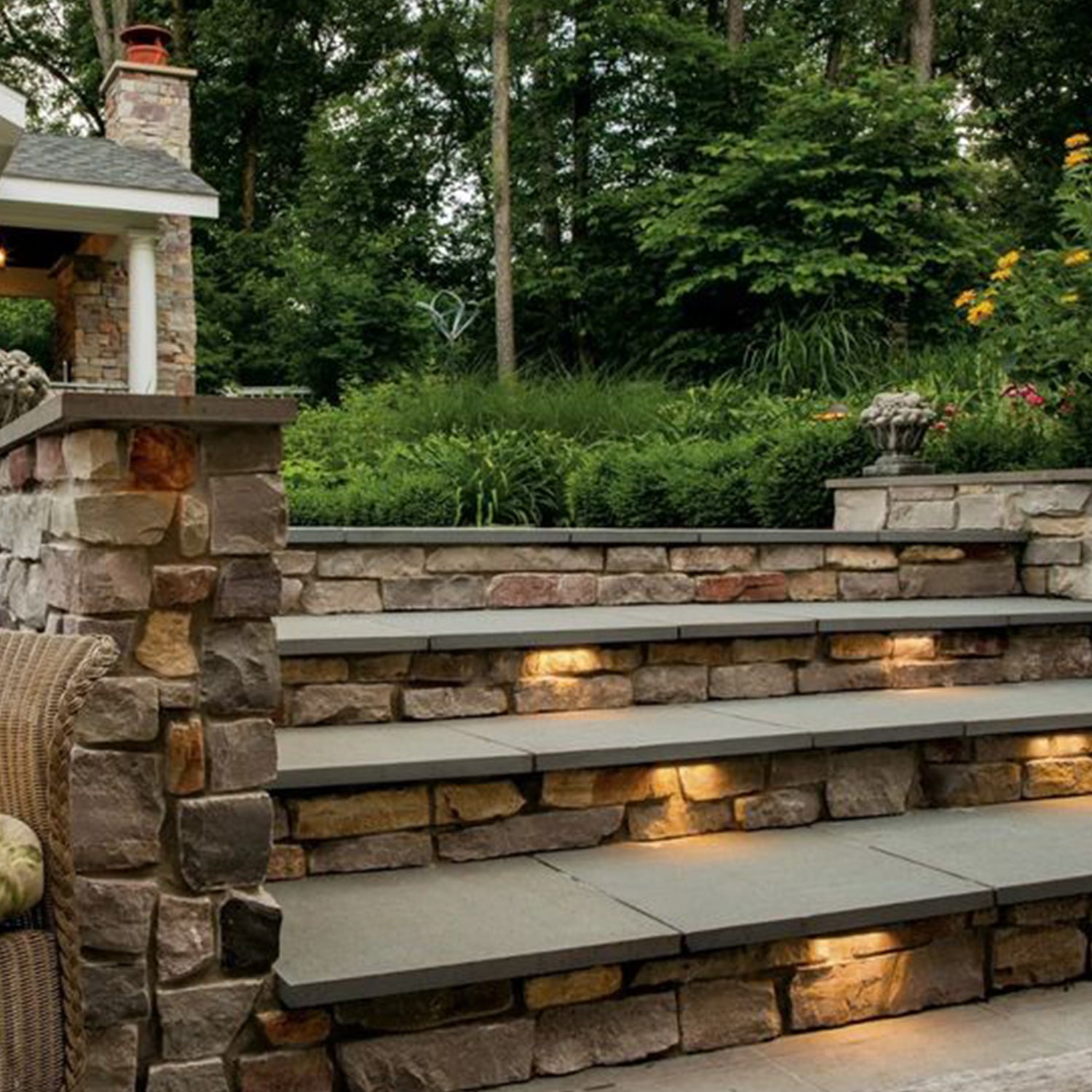 Outdoor stone staircase with integrated LED hardscape lights illuminating each step, surrounded by lush greenery and stone wall, showcasing durable and energy-efficient lighting solutions for outdoor spaces.