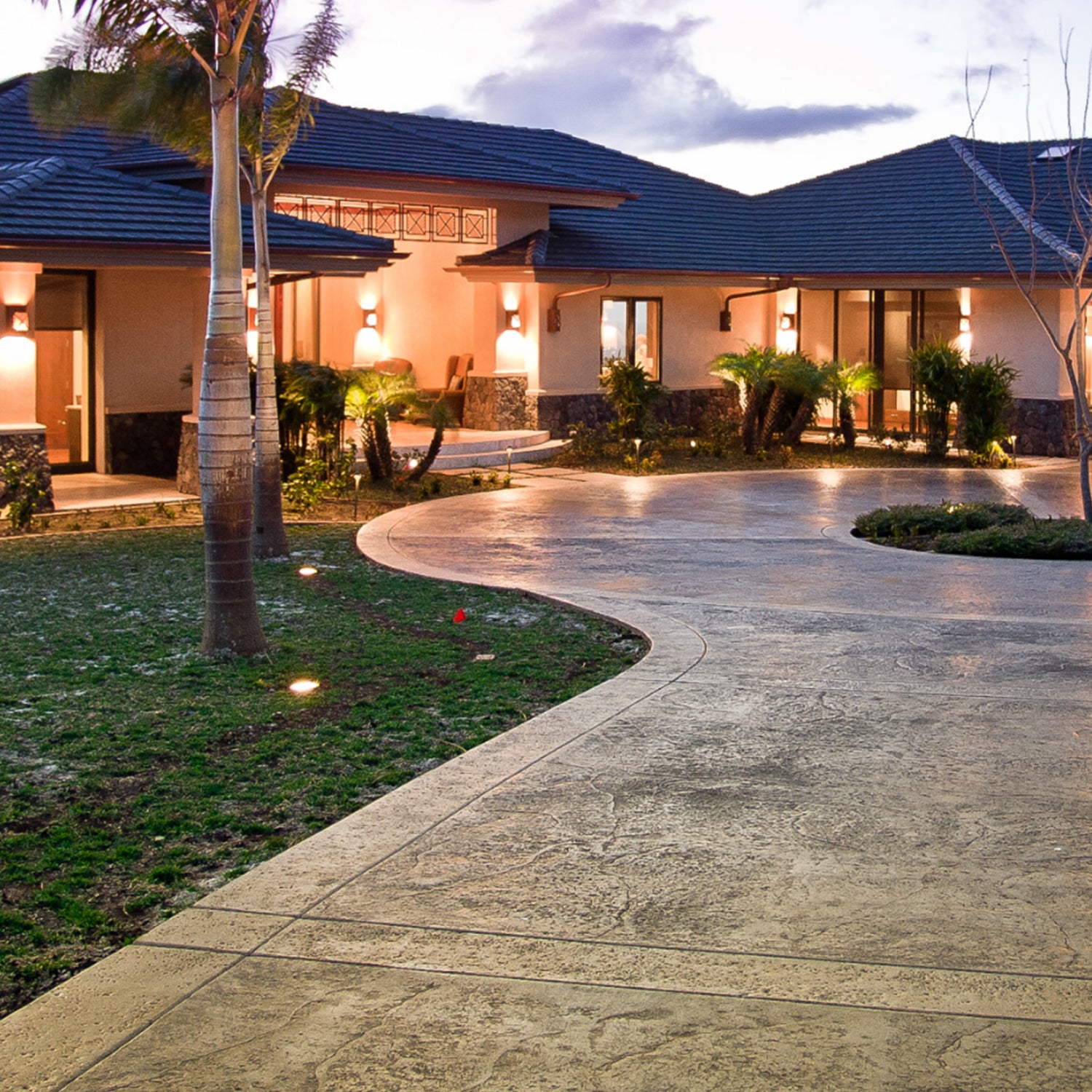 Elegant home with curved driveway and LED in-ground lights illuminating the landscape at dusk