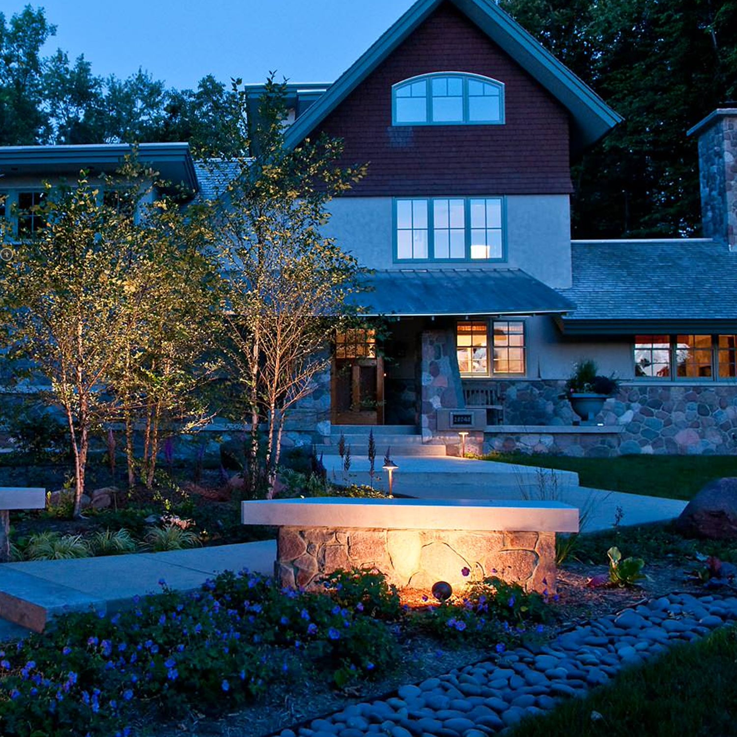 Nighttime landscape illuminated by brass LED flood lights, highlighting a modern house, garden, and architectural features