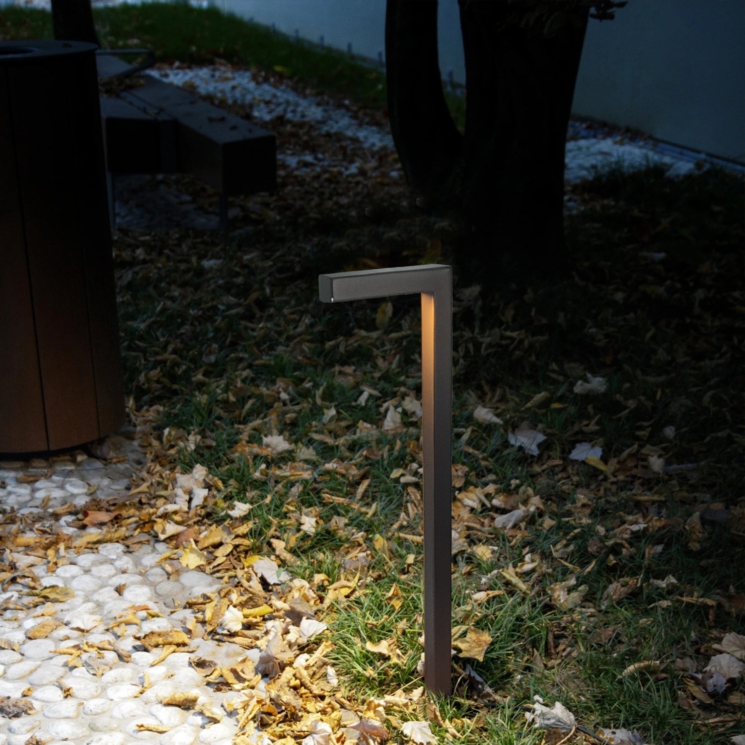 L-shaped low voltage brass path light illuminating garden walkway with fallen leaves, featured in serene outdoor setting at night